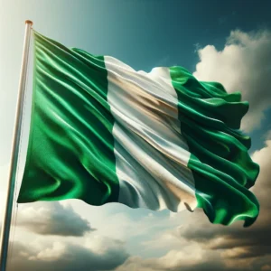 A photograph of a Nigerian flag, with its vibrant vertical green, white, and green stripes. The flag is depicted fluttering against a partly cloudy blue sky,